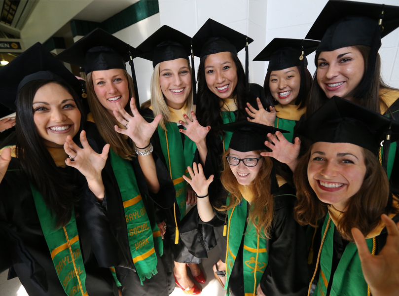 Graduates raise a "Sic 'Em" while dressed in graduate regalia.