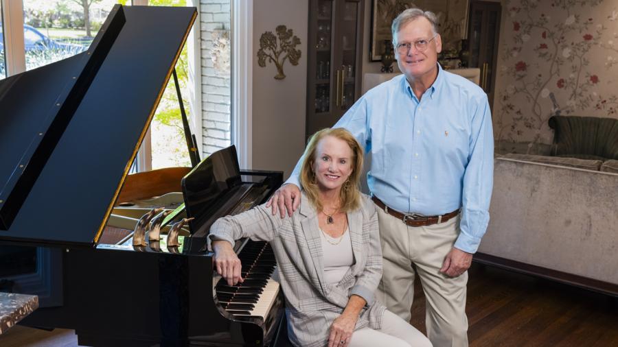 Christine and Jeffrey Klote sit a t a grand piano in their home and smile at the camera