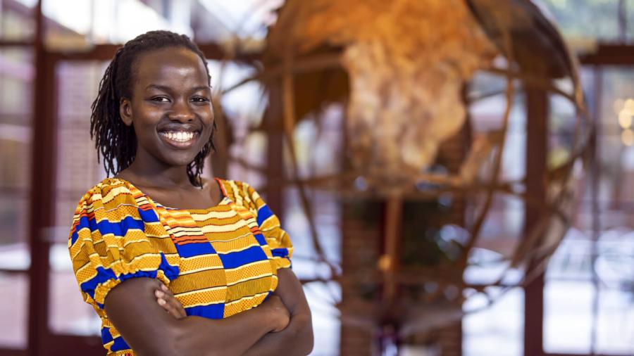 Revina Karani, dressed in yellow and white, stand smiling at the camera with a sculpture of a globe in the background