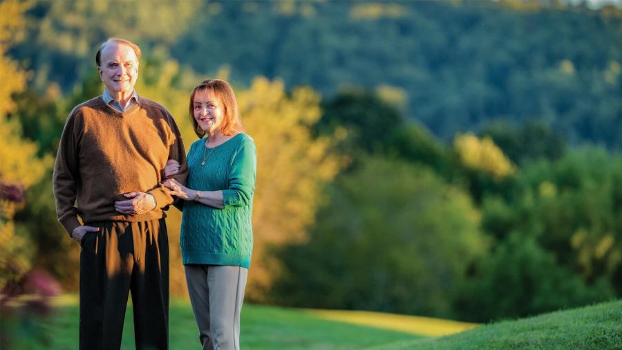 Photo of Gary and Barbara Grisham standing on a grassy hill, bathed in late afternoon sunlight